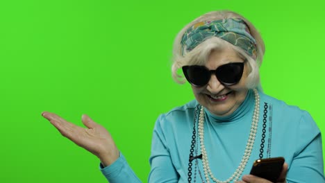 caucasian grandmother woman using smartphone, pointing at something with hand