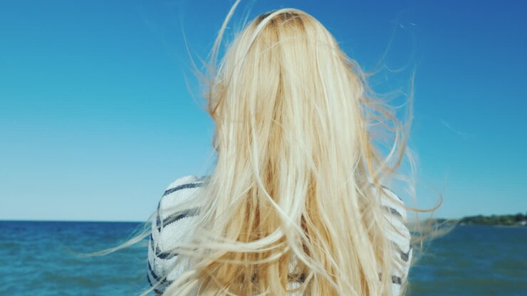 Donna Bionda Con Capelli Lunghi Guarda Il Mare, Il Vento Le Scompiglia I Capelli