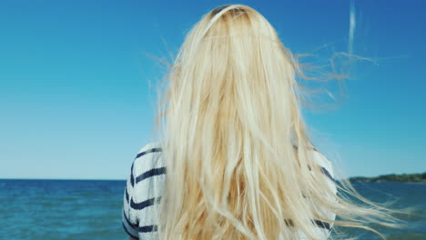 blonde woman with long hair looks at the sea wind ruffles her hair