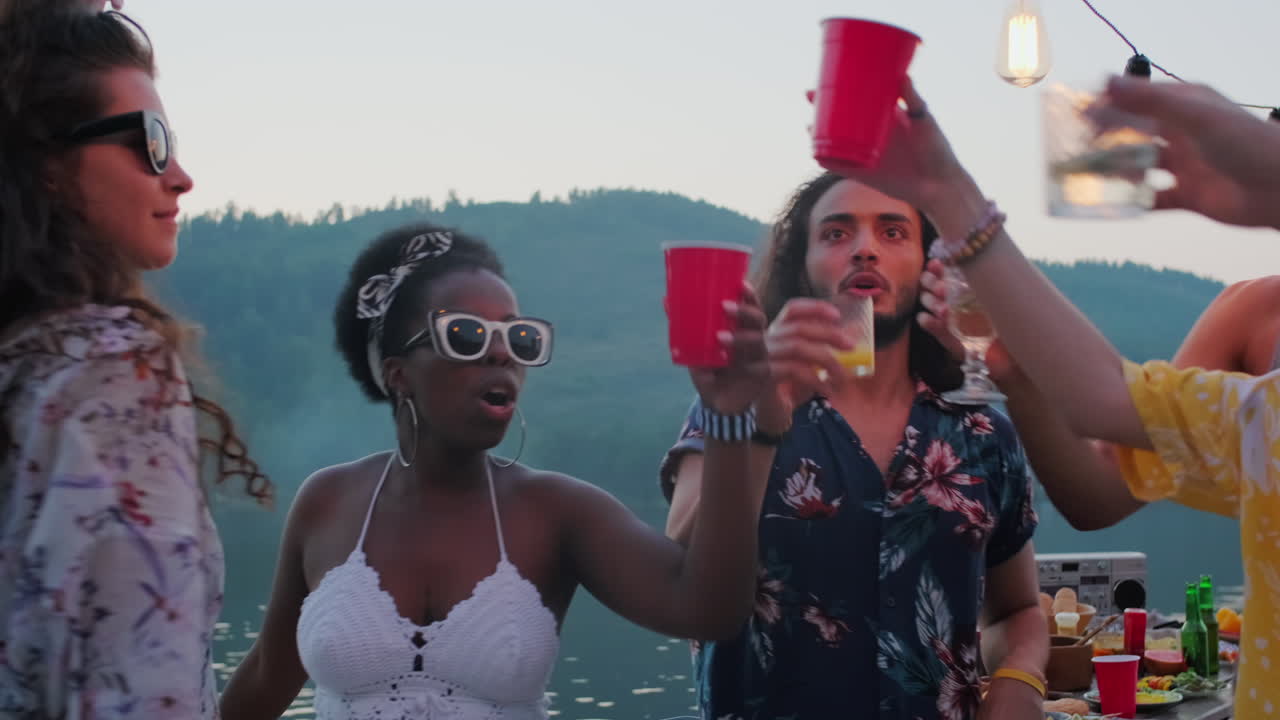 호수 파티에서 친구들이 춤을 추고 술을 마시며 토스트를 습니다.