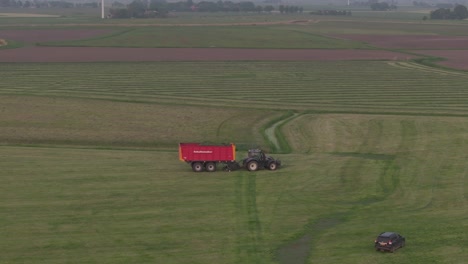 Tractor-driving-on-dutch-countryside-with-trailer-full-with-grass,-aerial