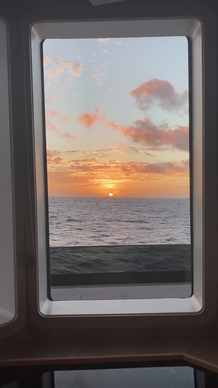 Filmato verticale da telefono del sole che tramonta all'orizzonte, visto attraverso i finestrini del ponte di un grande yacht in navigazione.