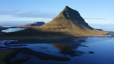 rising aerial view across kirkjufell mountain reflecting in calm blue sunset waters in snæfellsnes peninsula, iceland