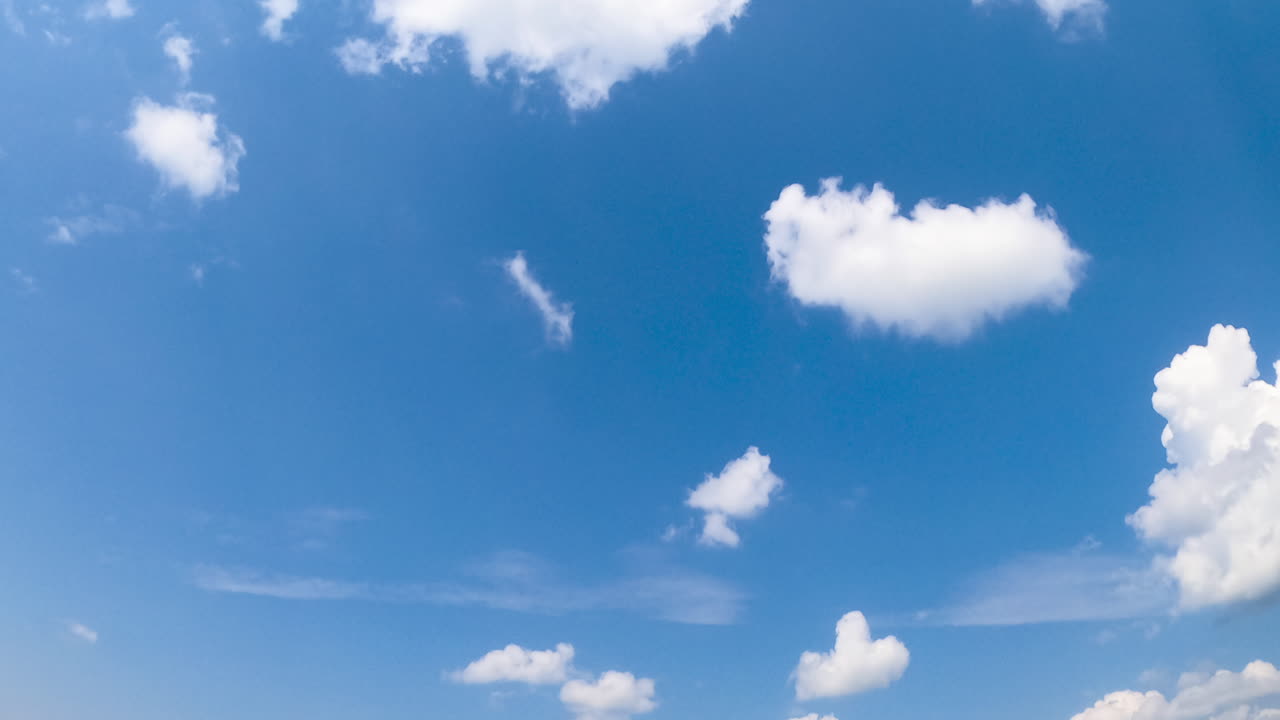 A few little white soft clouds in the sky change into bigger ones. Summer sky from low angle perspective. Timelapse.