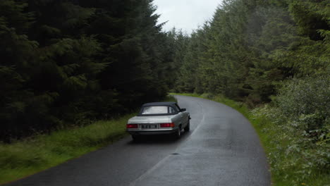 Vorwärtsverfolgung-Von-Oldtimer-Sportwagen,-Die-Auf-Schmaler,-Nasser-Straße-In-Dichtem-Wald-Fahren.-Regnerischer-Herbsttag.-Irland