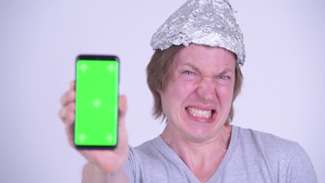 partidario de la teoría de la conspiración hombre con sombrero de aluminio y mostrando teléfono móvil con pantalla verde
