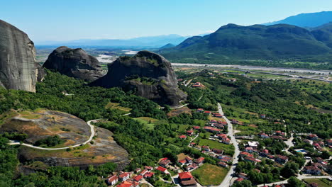 Aerial-drone-shot-of-a-town-at-the-foothills-of-Meteora-Monasteries-on-mountain-in-Greece-on-a-sunny-day