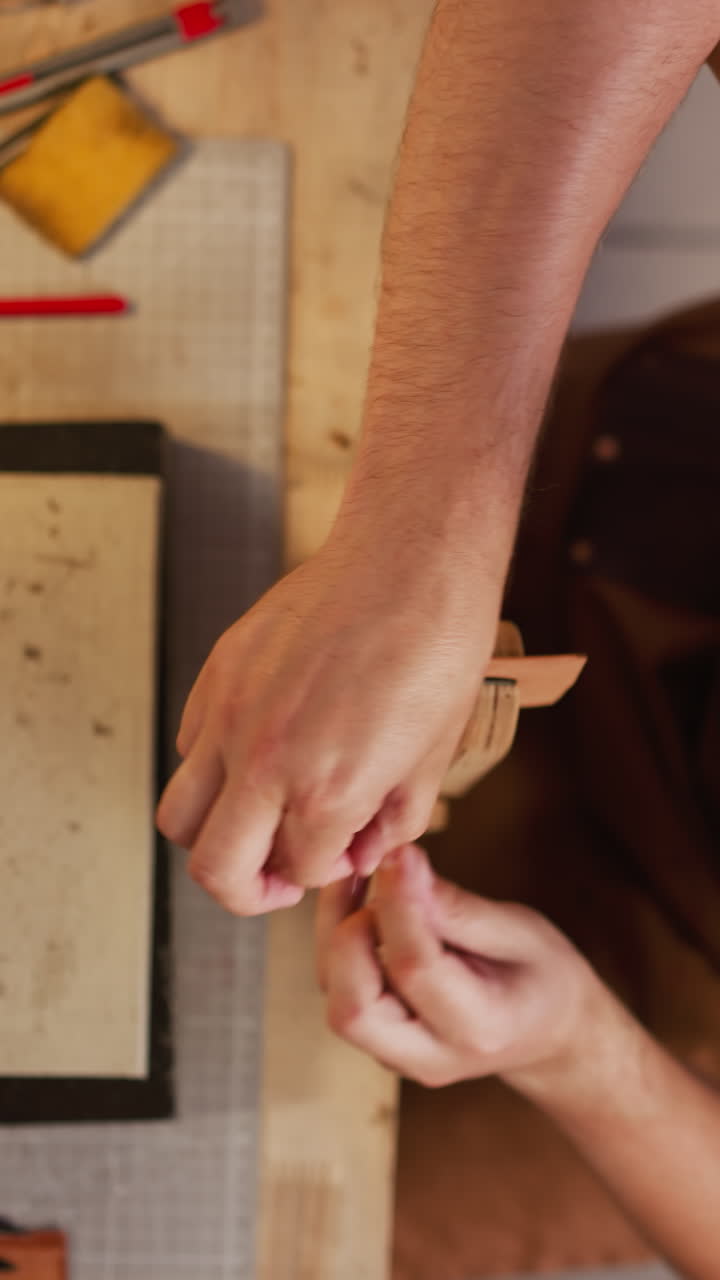 Skilled tailor sews leather item detail with waxed thread at table in craft workshop upper view. Accurate manual work. Craftsman at workplace
