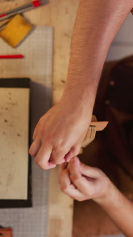 skilled tailor sews leather item detail with waxed thread at table in craft workshop upper view. accurate manual work. craftsman at workplace