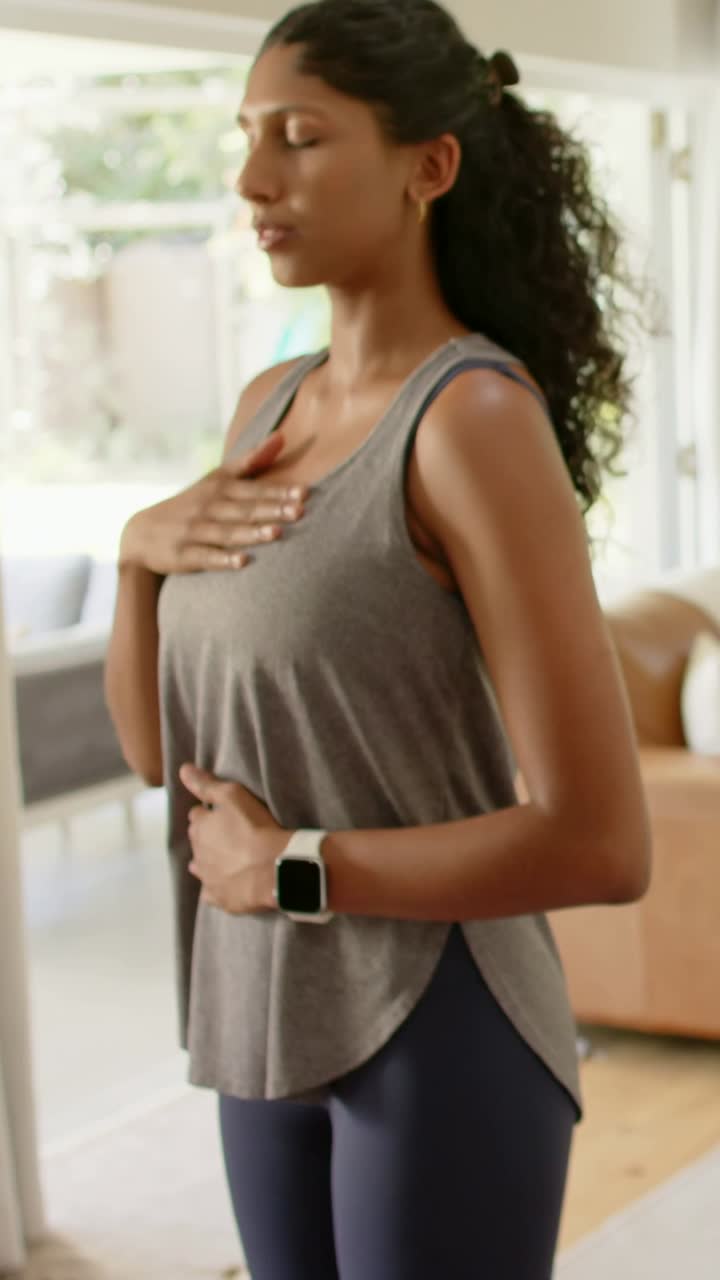 Video verticale: Donna in canottiera che inizia a respirare per calmarsi nel salotto indossando uno smartwatch.
