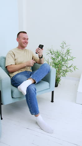 happy smiling man sits in the chair holding his phone. man's mood changes sad when he starts to use gadget. vertical video.