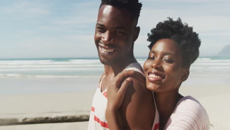 portrait of happy african american couple embracing on sunny beach