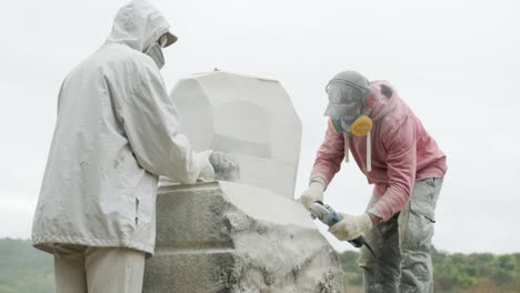 two sculptors create a statue of stone with a hammer and grinder