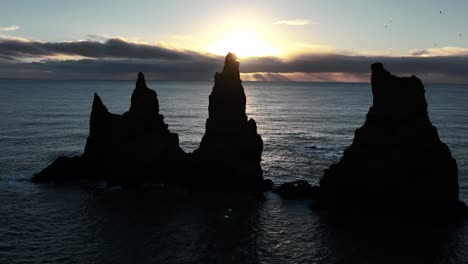 reynisdrangar sea stacks in silhouette at sunset in winter in south iceland. drone sideways shot