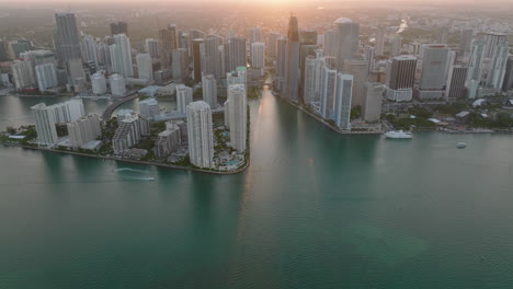 High-angle-view-of-high-rise-buildings-on-waterfront.-Tilt-up-reveal-modern-urban-borough-against-setting-sun.-Miami,-USA