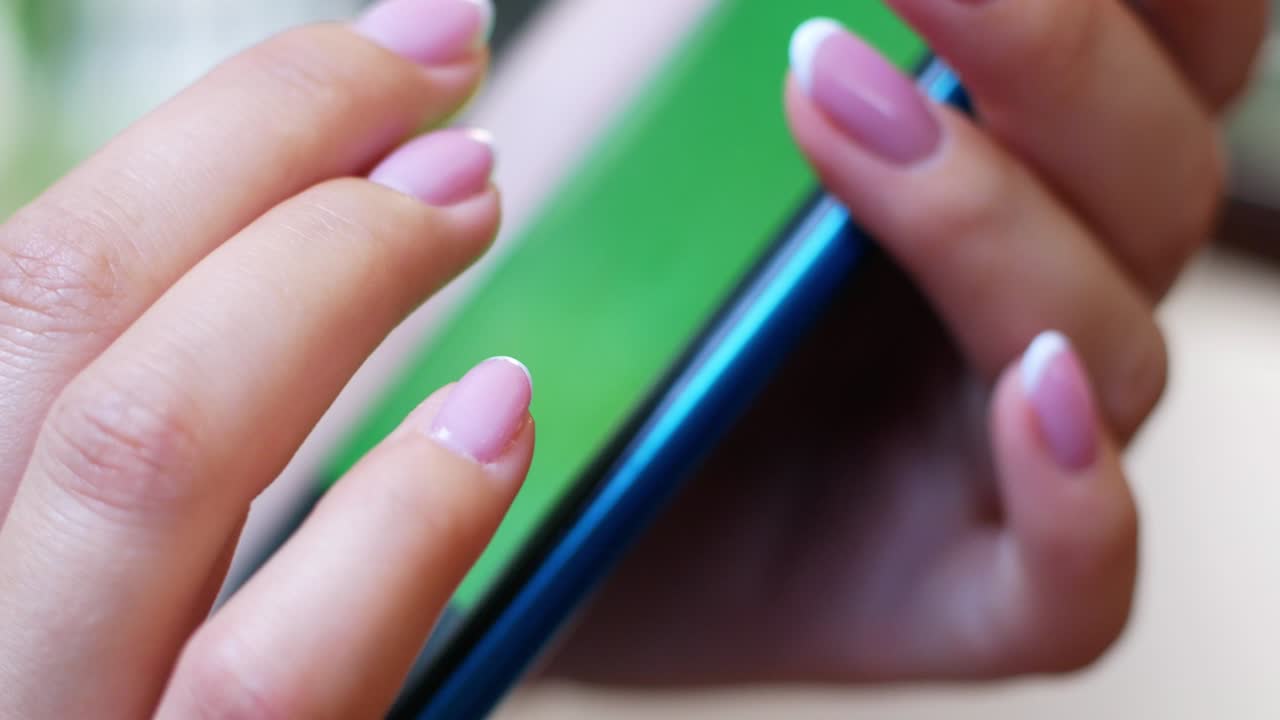 una mujer está sentada en un café con un teléfono inteligente en las manos con una maqueta de pantalla verde. la chica navega por internet, ve contenido, videos, blogs.