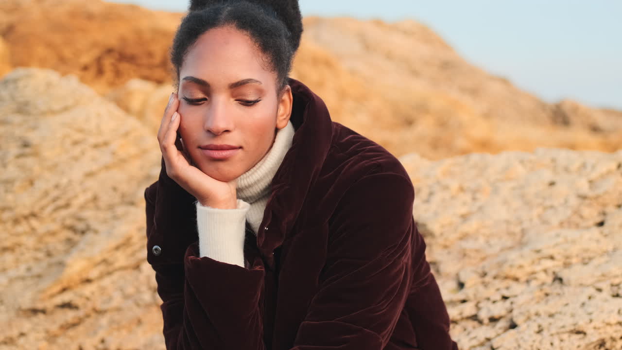 uma rapariga afro-americana sentada em pedras à beira-mar.