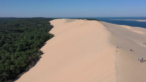 overview of dune du pilat sandhill in arcachon bassin france with people walking along the top ridge, aerial flyover shot