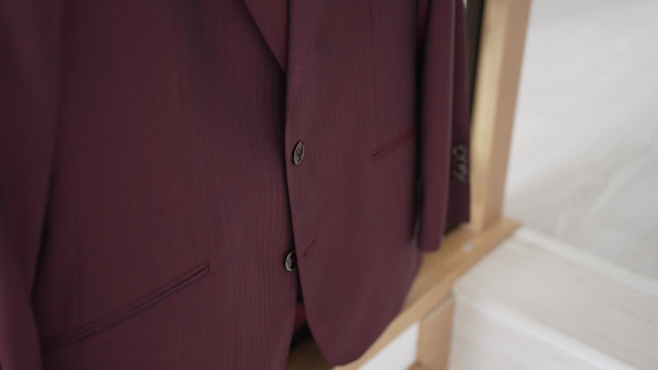 Close up of a burgundy suit jacket with buttons and pockets on a wooden hanger