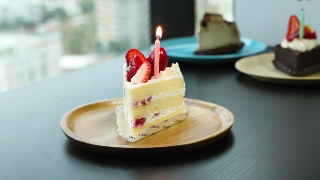 Hand lights candle on strawberry shortcake slice, natural daylight, shallow depth of field