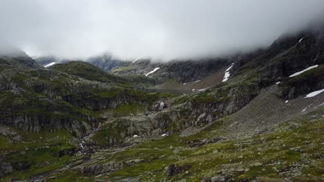 flying backwards from a lake with a waterfall, revealing a landscape with green grass, rocky hills with snow