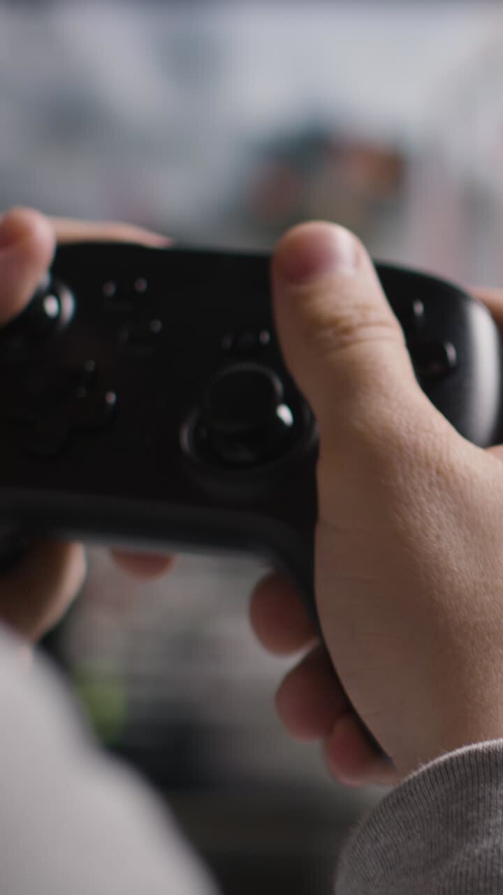 Video verticale, primo piano: mani di un uomo che gioca a un videogioco sparatutto con controller su schermo