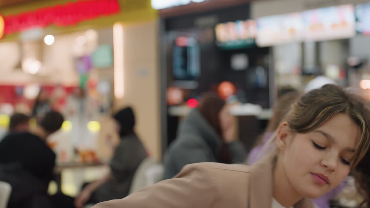 Улыбающаяся молодая женщина с подносом; жизнерадостная молодая женщина в блейзере, разносящая еду в фуд-корте; лучезарно улыбающаяся молодая женщина в повседневном блейзере, приветливо разносящая еду гостям в обеденной зоне