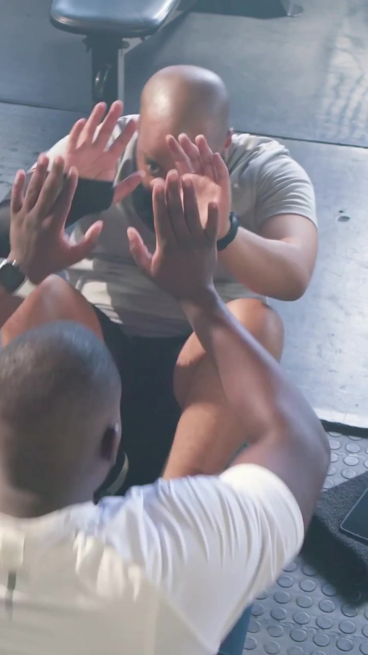 Vertical video: Partner bracing feet, man in grey tee doing situps on gym mat for fitness