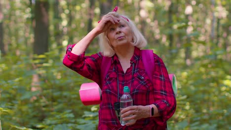 Tired-thirsty-senior-old-Caucasian-hiker-grandmother-relaxing,-drinking-water-in-forest-after-walk