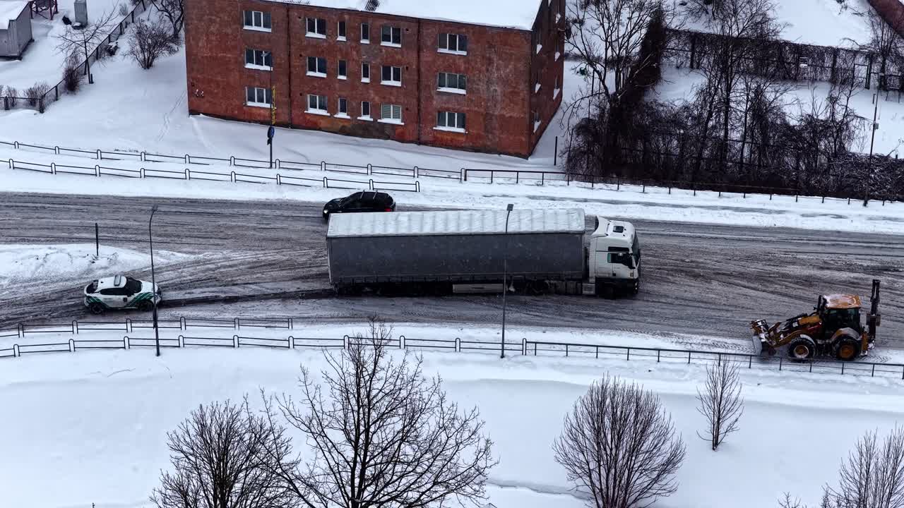 Semi truck navigating icy road in winter, not able to drive uphill and getting stuck, aerial drone hyperlapse