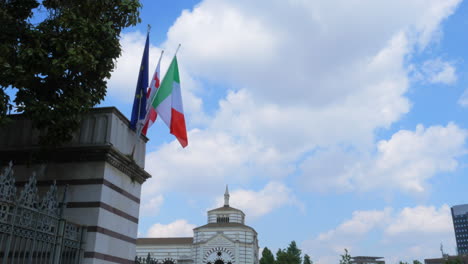 italian, european and milanese flag waving near the cementry in milan