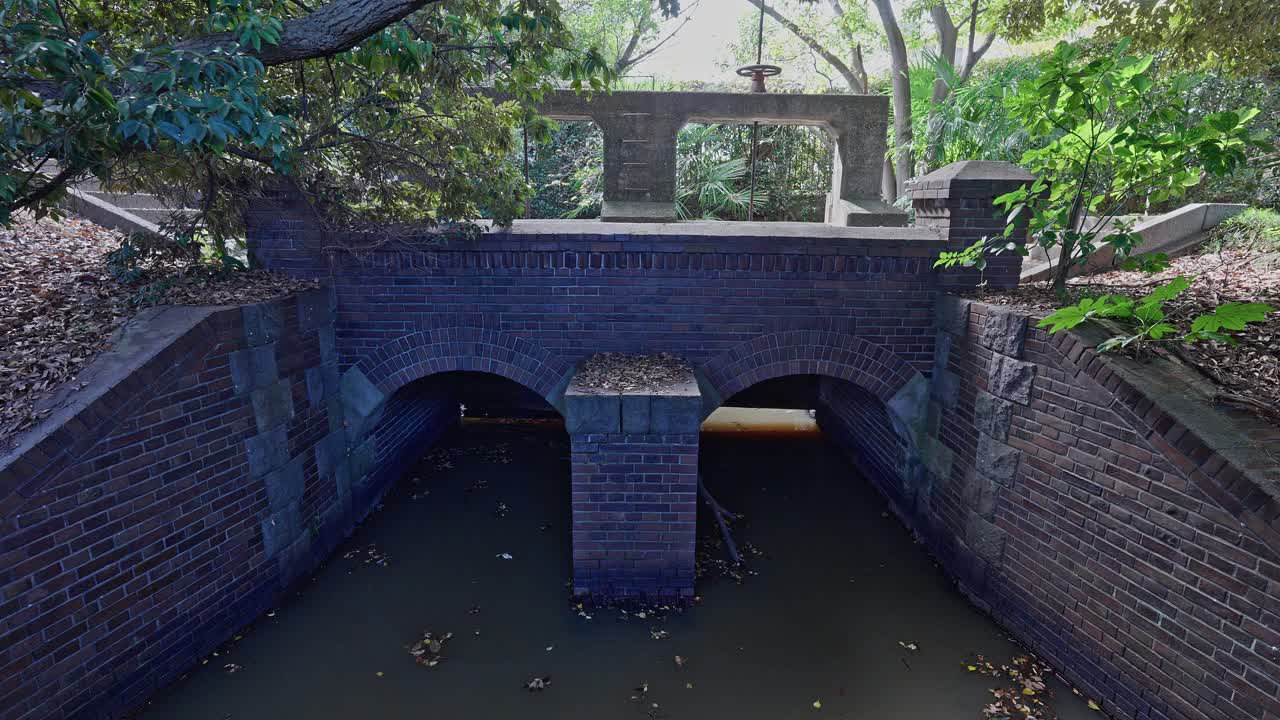 The dark brick culvert of the Jinzaemon Weir with two archways carrying water, leading toward the concrete gate structure
