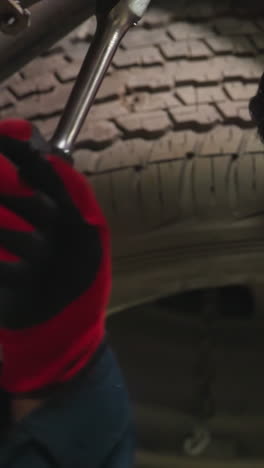 ingeniero indio que trabaja debajo de un coche, apretando el perno con expresión enfocada, la luz se refleja en la cara, usando guantes y uniforme azul, involucrado en la reparación de automóviles, inspeccionando la mecánica de vehículos