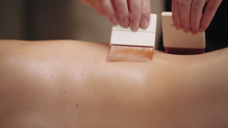 spa treatment for relaxation massage with brushes masseuse is stroking back of patient by soft brush