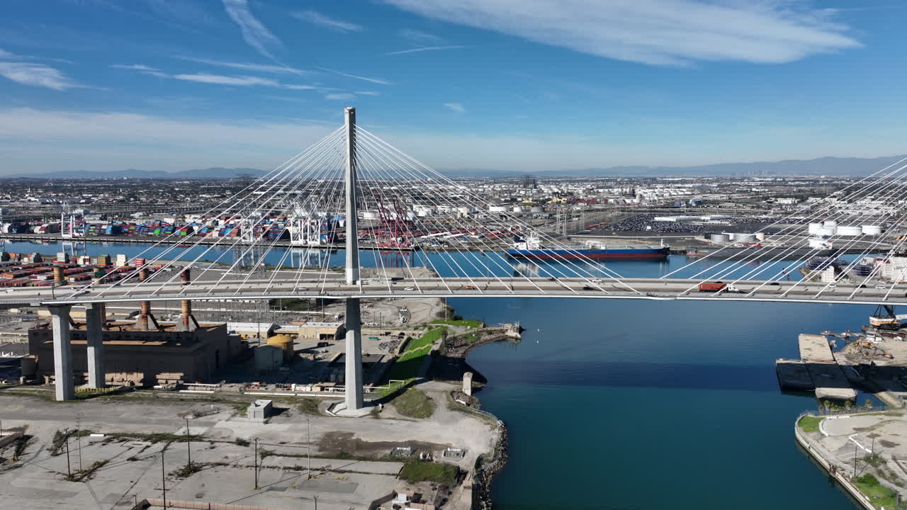 Sunny drone view of the International Gateway Bridge near Terminal Island highlighting container yards, commercial trucking, and the busy port environment