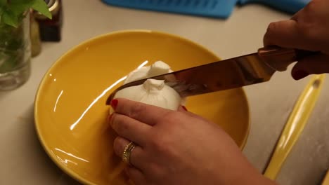 slicing a fresh baby mozzarella ball in half to use in a salad - slow motion isolated