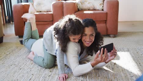 madre e hija de raza mixta felices acostadas en el suelo, divirtiéndose y tomando selfies