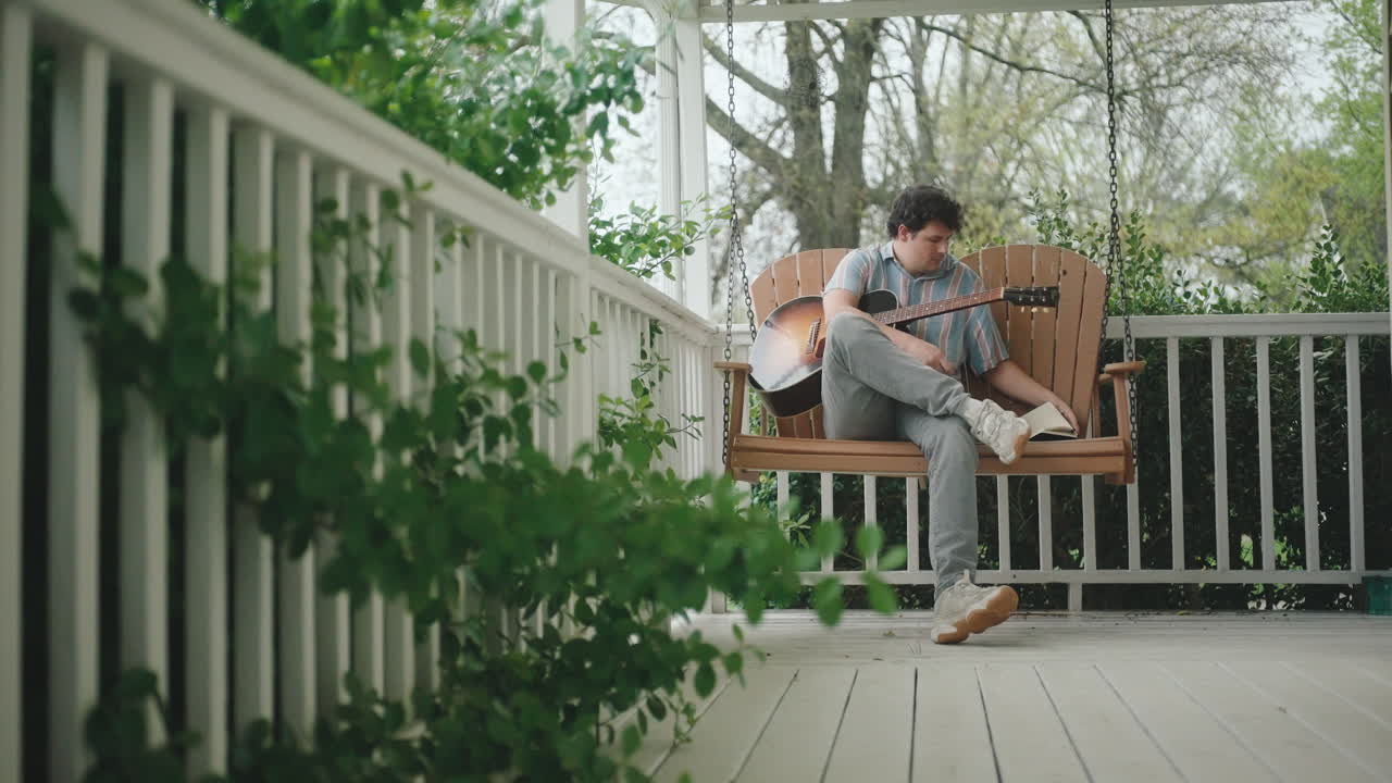 Mand spiller guitar og skriver på en verandagynge