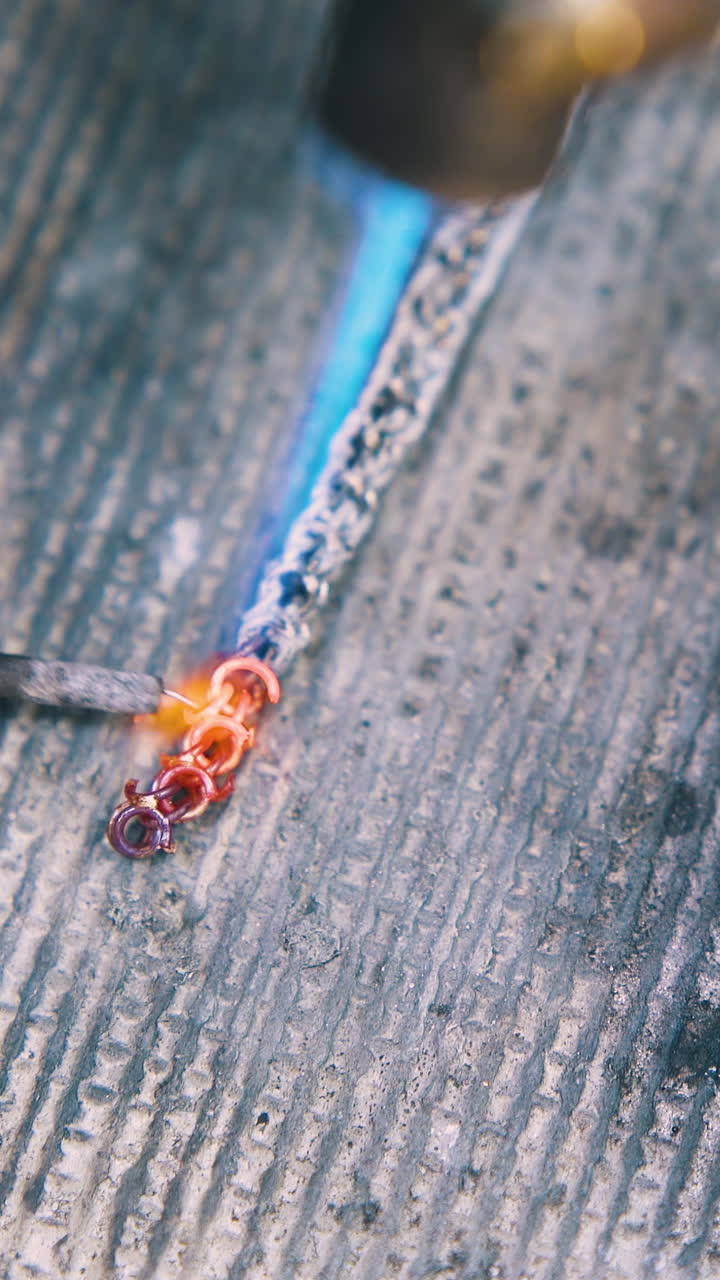 CU: experienced jeweler welds links of decorative gold metal chain on fireproof asbestos sheet close upper view