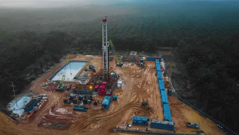 toma cinematográfica de drones de perforación en tierra y estructura de plataforma de reacondicionamiento y equipo de plataforma para exploración y explotación de petróleo en medio de la jungla rodeada de palmeras durante la puesta de sol