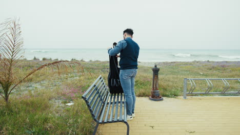 man with guitar case on a beach bench