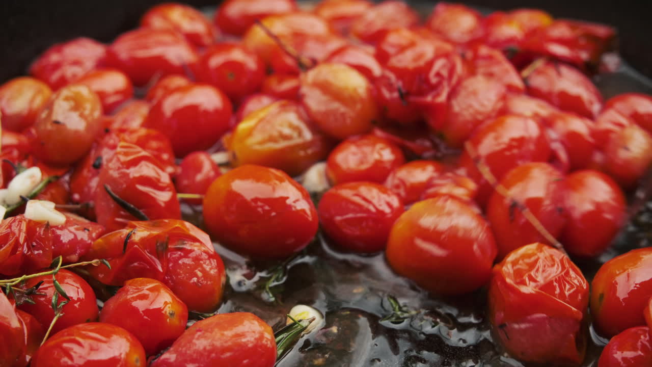 Close-up juicy saut&eacute;ed cherry tomatoes sizzling in a cast-iron skillet with herbs and garlic