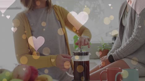 Animation-of-hearts-over-caucasian-female-couple-making-coffee
