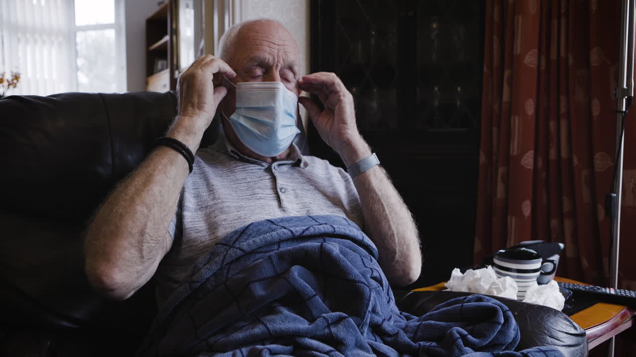 Elderly man with a mask in a chair covered with a blanket