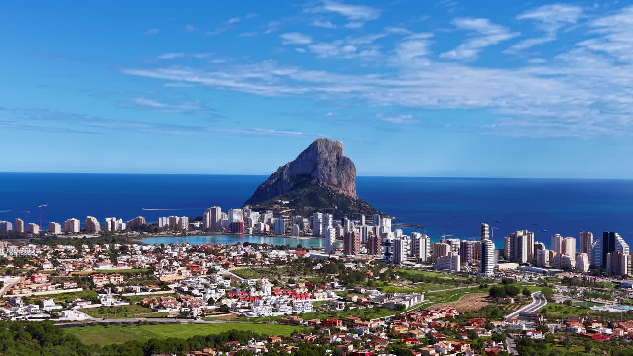 Panoramatický pohled na Calpe ve Španělsku, s ikonickým skalním útvarem Penon de Ifach tyčícím se nad pobřežním městem a Středozemním mořem v pozadí.
