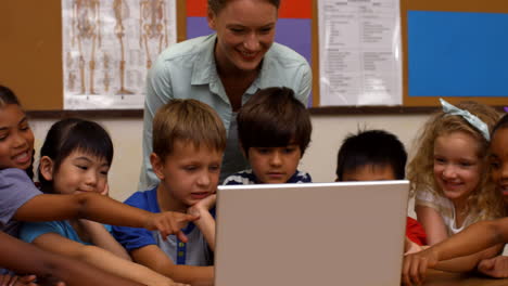 Lindos-Alumnos-Mirando-La-Computadora-Portátil-Con-El-Maestro