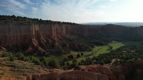 Aerial-drone-view-flying-backward-from-a-green-valley-to-a-red-dessert,-backlight