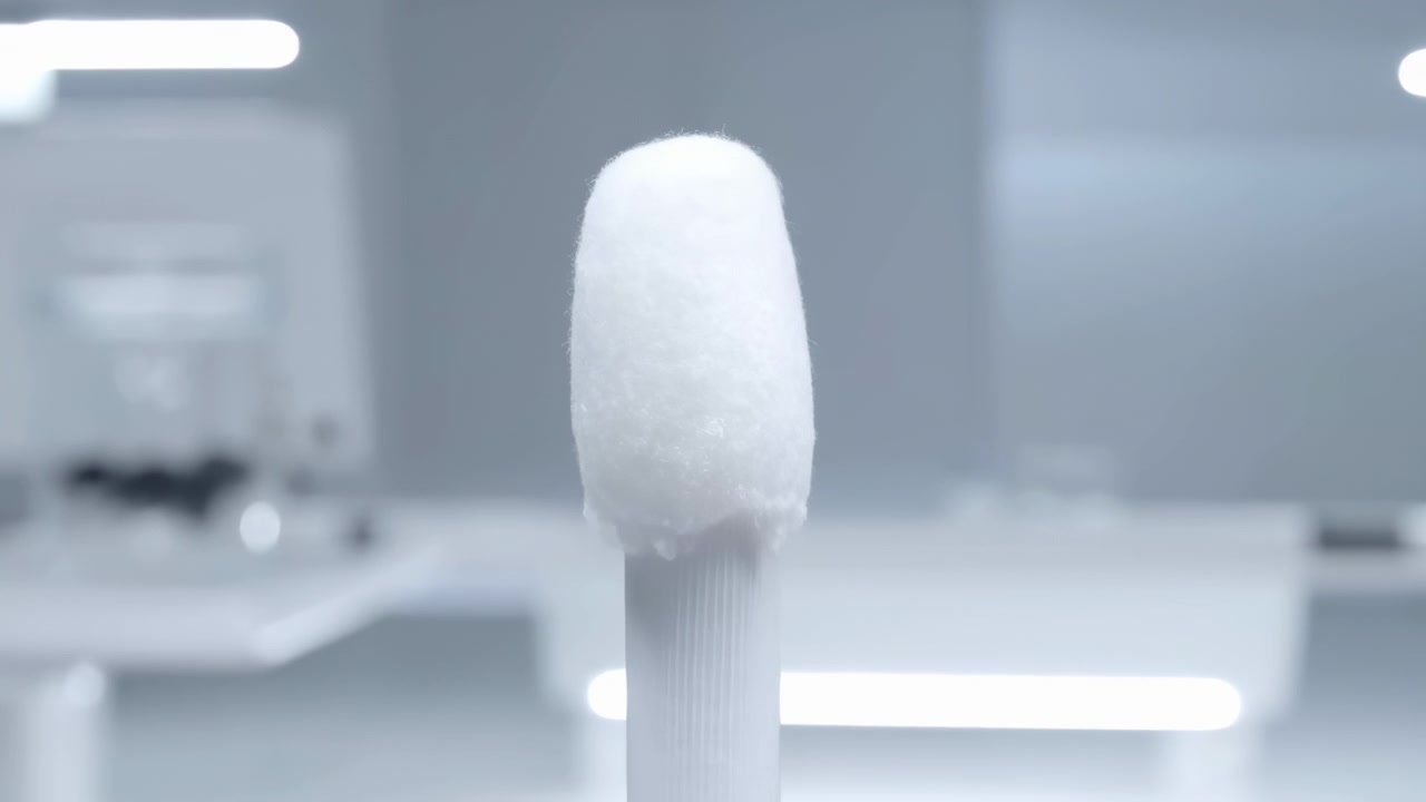 Front-facing close-up shows white foam swab tip on textured plastic handle, centered upright inside sterile clinical or laboratory interior with soft blur, cool light, symmetry, clean detail