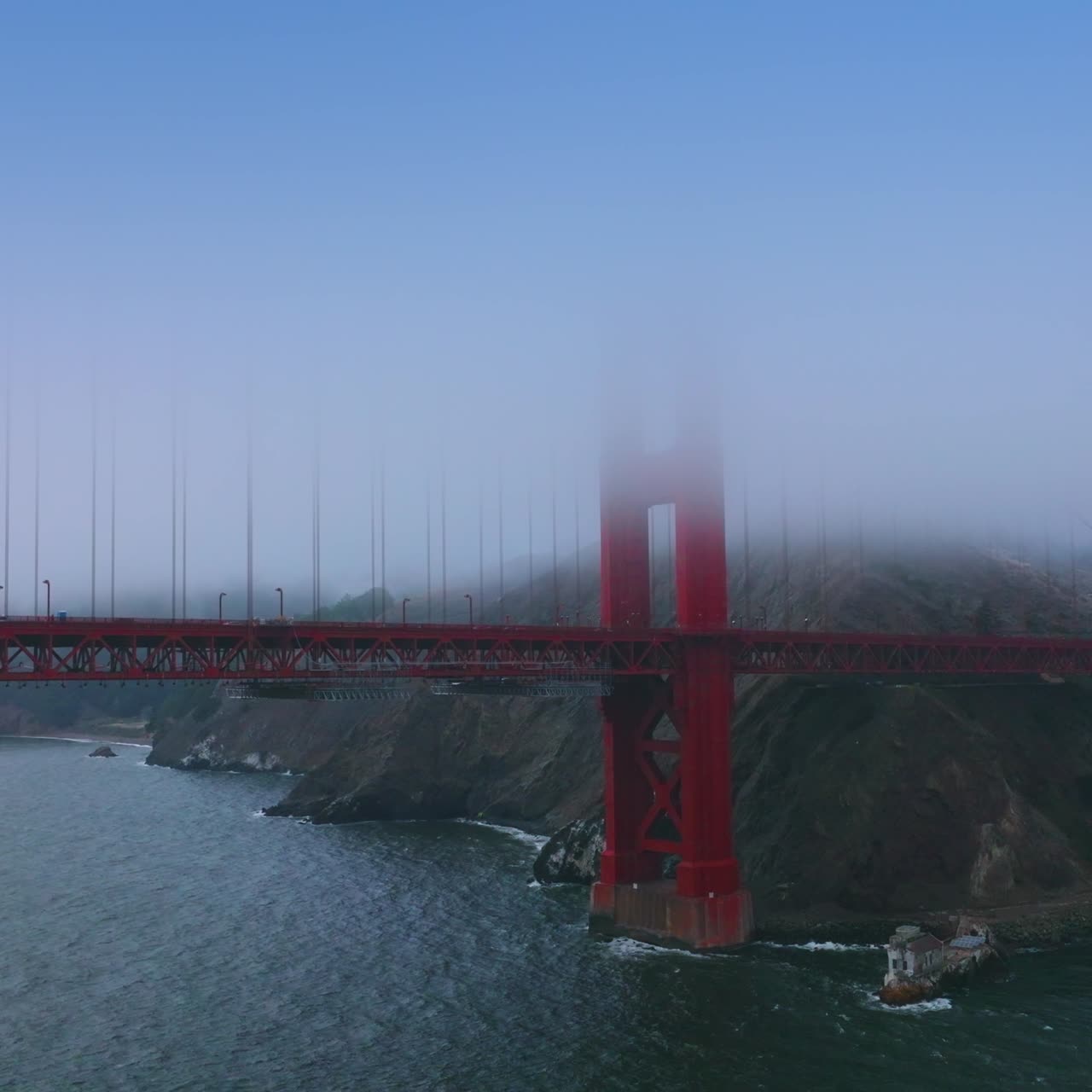 Quickly moving cars by the huge bridge of Golden Gate Straight in San Francisco, California. Approaching the bridge partially hidden in the mist