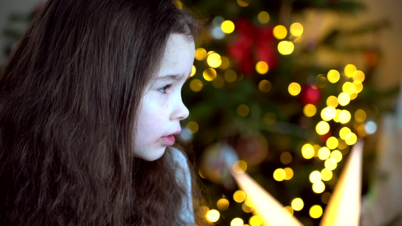 크리스마스 트리 근처에 앉아있는 행복한 어린 소녀의 초상화 새해 전날 꾸며진 방에서 새해와 휴일과 어린이 개념과 함께 축제 휴일 축제를 즐기고 있습니다.